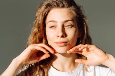 Sıcak bir odada otururken yüzüne dokunan sevimli bir kadının portresi. Güneş ışınlarının ve doğal güzelliğin tadını çıkaran güzel bir kadın. Doğal güzellik, dermatoloji ve kozmetoloji kavramı.