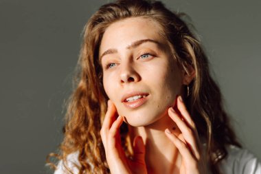 Sıcak bir odada otururken yüzüne dokunan sevimli bir kadının portresi. Güneş ışınlarının ve doğal güzelliğin tadını çıkaran güzel bir kadın. Doğal güzellik, dermatoloji ve kozmetoloji kavramı.