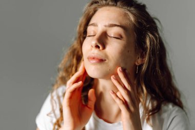 Sıcak bir odada otururken yüzüne dokunan sevimli bir kadının portresi. Güneş ışınlarının ve doğal güzelliğin tadını çıkaran güzel bir kadın. Doğal güzellik, dermatoloji ve kozmetoloji kavramı.