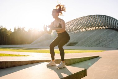 Spor giyim sektöründe dinamik antrenman yapan, gün batımında atlayan bir kadın. Parkta güneşin altında antrenman yapan genç bir sporcu. Spor, aktivite ve atlama kavramı. Etkin yaşam biçimi.