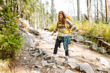 Dağlarda yürüyen kayalık bir patikada renkli bir sırt çantasıyla kadın yürüyüşçü. Yoğun bir ormanda dağ manzarasından hoşlanan sevimli bir kadın. Macera, yürüyüş ve doğa konsepti.