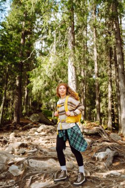 Dağlarda yürüyen kayalık bir patikada renkli bir sırt çantasıyla kadın yürüyüşçü. Yoğun bir ormanda dağ manzarasından hoşlanan sevimli bir kadın. Macera, yürüyüş ve doğa konsepti.