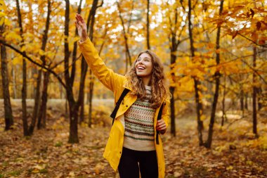 Genç bir kadın sonbahar parkında eğleniyor, sarı yapraklar saçıyor. Parlak yağmurluklu kadın gezgin gün batımında ormanda güzel bir yolda yürüyor. Mevsimlik kavramı, sonbahar