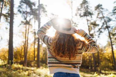 Şapkalı genç bir kadın gülerek sonbahar parkında güneşli bir günün tadını çıkarıyor. Dışarıda yürüyen mutlu bir kadın. Aktif yaşam tarzı. Yürüyüş ve doğa konsepti.