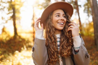 Şapkalı genç bir kadın gülerek sonbahar parkında güneşli bir günün tadını çıkarıyor. Dışarıda yürüyen mutlu bir kadın. Aktif yaşam tarzı. Yürüyüş ve doğa konsepti.