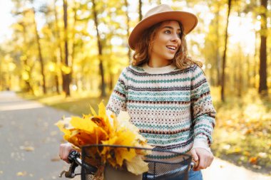 Sessiz bir sonbahar ormanında bisiklet süren neşeli bir kadın. Genç bir kadın yürüyüş yapıyor ve bisikletle eğleniyor. Etkin yaşam biçimi.