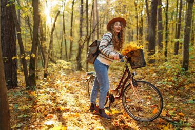 Sessiz bir sonbahar ormanında bisiklet süren neşeli bir kadın. Genç bir kadın yürüyüş yapıyor ve bisikletle eğleniyor. Etkin yaşam biçimi.
