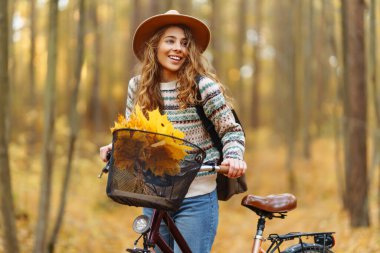 Sessiz bir sonbahar ormanında bisiklet süren neşeli bir kadın. Genç bir kadın yürüyüş yapıyor ve bisikletle eğleniyor. Etkin yaşam biçimi.