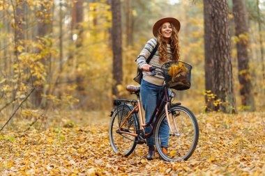 Sessiz bir sonbahar ormanında bisiklet süren neşeli bir kadın. Genç bir kadın yürüyüş yapıyor ve bisikletle eğleniyor. Etkin yaşam biçimi.