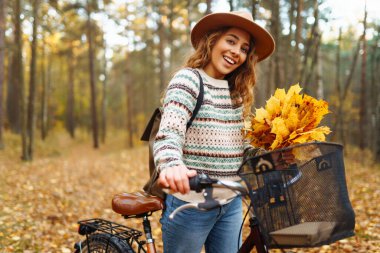 Sessiz bir sonbahar ormanında bisiklet süren neşeli bir kadın. Genç bir kadın yürüyüş yapıyor ve bisikletle eğleniyor. Etkin yaşam biçimi.