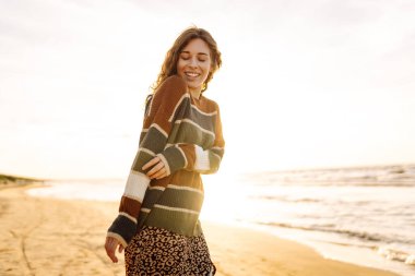 Şapkalı neşeli kadın güneşli sahilde eğleniyor ve yürüyor. Özgürlüğü hisseden ve deniz manzarasının tadını çıkaran güzel bir kadın. Özgürlük, rahatlama konsepti. Yaşam biçimi.