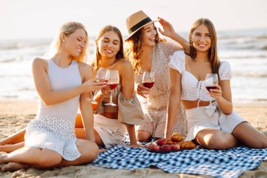 Deniz kıyısında piknik yapan neşeli kadınlar birlikte vakit geçiriyorlar, doğada dinleniyorlar. Dört kız arkadaş eğleniyor, şarap içiyor ve açık havada gün batımıyla buluşuyorlar. Dostluk kavramı, kutlama.