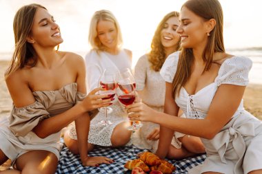 Deniz kıyısında piknik yapan neşeli kadınlar birlikte vakit geçiriyorlar, doğada dinleniyorlar. Dört kız arkadaş eğleniyor, şarap içiyor ve açık havada gün batımıyla buluşuyorlar. Dostluk kavramı, kutlama.