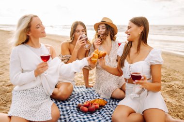 Deniz kıyısında piknik yapan neşeli kadınlar birlikte vakit geçiriyorlar, doğada dinleniyorlar. Dört kız arkadaş eğleniyor, şarap içiyor ve açık havada gün batımıyla buluşuyorlar. Dostluk kavramı, kutlama.