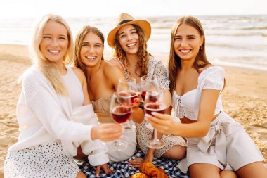 Deniz kıyısında piknik yapan neşeli kadınlar birlikte vakit geçiriyorlar, doğada dinleniyorlar. Dört kız arkadaş eğleniyor, şarap içiyor ve açık havada gün batımıyla buluşuyorlar. Dostluk kavramı, kutlama.