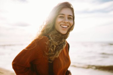 Kazaklı ve sırt çantalı sakin bir kadın rıhtımda deniz esintisinin ve temiz havada gün batımının tadını çıkarıyor. Güzel bir kadın doğada kendini özgür ve rahat hisseder. Doğa konsepti, rahatlama..