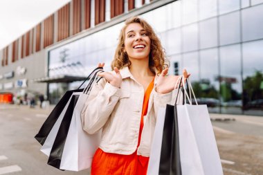 Modern alışveriş merkezinin önünde şık kıyafetler içinde güzel bir kadın. Alışverişten sonra dışarıda gezen neşeli bir kadın. Tüketim kavramı, indirimler.