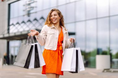 Modern alışveriş merkezinin önünde şık kıyafetler içinde güzel bir kadın. Alışverişten sonra dışarıda gezen neşeli bir kadın. Tüketim kavramı, indirimler.