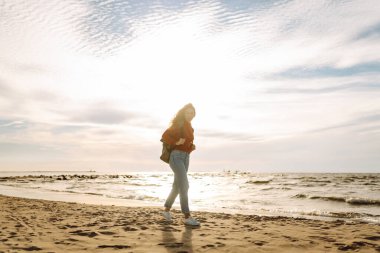 Evrak çantalı tatlı bir kadın deniz kıyısında ya da okyanusta duruyor ve günbatımının tadını çıkarıyor. Gezgin açık havada özgürlüğü hissediyor. Macera, doğa konsepti. Yaşam biçimi.