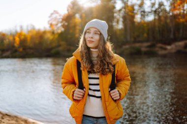 Sonbaharda yürüyüş parkurunda sırt çantasıyla gezen genç bir bayan yürüyüşçünün güneş ışığının tadını çıkarırken görüntüsü. Güzel bir kadın kendini özgür hisseder ve sonbahar parkında yürür. Özgürlük kavramı, macera.