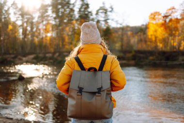 Sonbaharda yürüyüş parkurunda sırt çantasıyla gezen genç bir bayan yürüyüşçünün güneş ışığının tadını çıkarırken görüntüsü. Güzel bir kadın kendini özgür hisseder ve sonbahar parkında yürür. Özgürlük kavramı, macera.