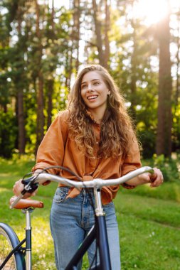 Yoğun güneşli bir ormanda bisiklet süren genç bir kadın. Doğanın tadını çıkaran ve gün batımında bisiklet süren mutlu bir kadın. Hafta sonu konsepti. Etkin yaşam biçimi.
