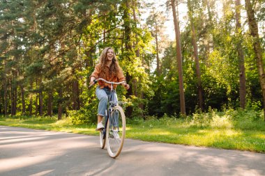 Yoğun güneşli bir ormanda bisiklet süren genç bir kadın. Doğanın tadını çıkaran ve gün batımında bisiklet süren mutlu bir kadın. Hafta sonu konsepti. Etkin yaşam biçimi.