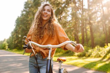 Yoğun güneşli bir ormanda bisiklet süren genç bir kadın. Doğanın tadını çıkaran ve gün batımında bisiklet süren mutlu bir kadın. Hafta sonu konsepti. Etkin yaşam biçimi.
