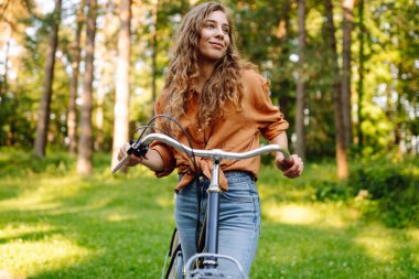 Yoğun güneşli bir ormanda bisiklet süren genç bir kadın. Doğanın tadını çıkaran ve gün batımında bisiklet süren mutlu bir kadın. Hafta sonu konsepti. Etkin yaşam biçimi.