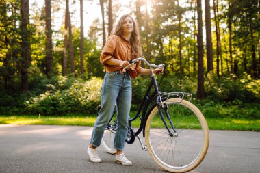 Yoğun güneşli bir ormanda bisiklet süren genç bir kadın. Doğanın tadını çıkaran ve gün batımında bisiklet süren mutlu bir kadın. Hafta sonu konsepti. Etkin yaşam biçimi.