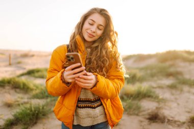 Sahile giden yolda telefonu olan kadın yürüyüşçünün portresi. Genç bir kadın gün doğumundan ve deniz manzaralı akıllı telefondan mesaj atmaktan hoşlanıyor. Macera ve teknoloji kavramı.