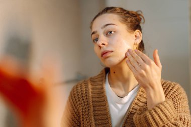 Aynadaki yansıması banyoda cilt bakımı yapan genç bir kadın. Güzel bir kadın yüzüne dokunuyor, kapalı alanda inceliyor. Güzellik konsepti, dikkat. Yaşam biçimi.