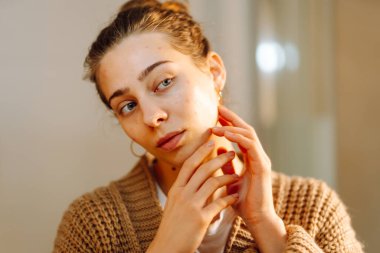 Aynadaki yansıması banyoda cilt bakımı yapan genç bir kadın. Güzel bir kadın yüzüne dokunuyor, kapalı alanda inceliyor. Güzellik konsepti, dikkat. Yaşam biçimi.