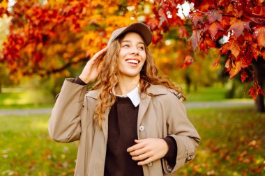 Mutlu kadın güneşli bir sonbahar parkında bir buket parlak yaprakla eğleniyor. Günbatımının tadını çıkaran günlük giysiler içinde güzel bir turist. Yürüme konsepti. Sonbahar atmosferi.