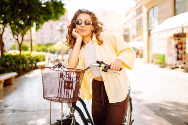 Neşeli bir turist şehrin güneşli caddelerinde bisiklet sürüyor. Güneş gözlüklü güzel bir kadın gün batımında bisiklet sürmekten hoşlanır. Turizm kavramı, eko taşımacılık.