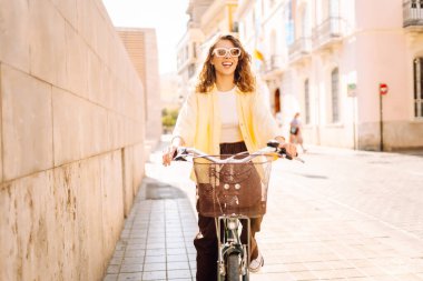 Neşeli bir turist şehrin güneşli caddelerinde bisiklet sürüyor. Güneş gözlüklü güzel bir kadın gün batımında bisiklet sürmekten hoşlanır. Turizm kavramı, eko taşımacılık.