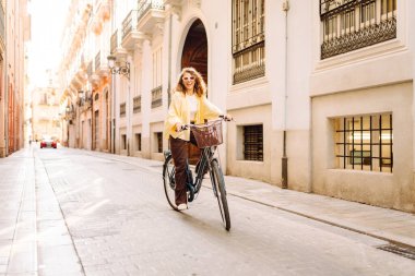 Neşeli bir turist şehrin güneşli caddelerinde bisiklet sürüyor. Güneş gözlüklü güzel bir kadın gün batımında bisiklet sürmekten hoşlanır. Turizm kavramı, eko taşımacılık.