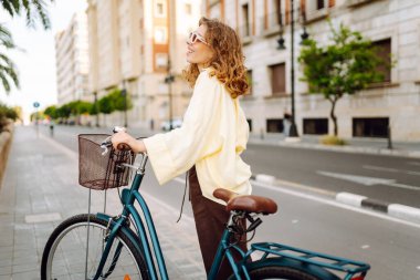 Neşeli bir turist şehrin güneşli caddelerinde bisiklet sürüyor. Güneş gözlüklü güzel bir kadın gün batımında bisiklet sürmekten hoşlanır. Turizm kavramı, eko taşımacılık.