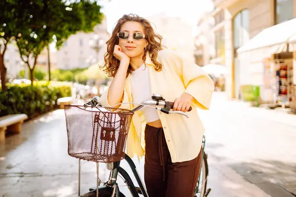 Neşeli bir turist şehrin güneşli caddelerinde bisiklet sürüyor. Güneş gözlüklü güzel bir kadın gün batımında bisiklet sürmekten hoşlanır. Turizm kavramı, eko taşımacılık.