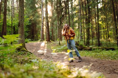 Sarı sırt çantalı bir yürüyüşçü güneşli ormanda yürüyüş yolunda yürüyor. Neşeli kadın gün batımında yürüyüş ve doğanın tadını çıkarıyor. Yürüyüş kavramı, doğa..
