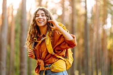 Sarı sırt çantalı bir yürüyüşçü güneşli ormanda yürüyüş yolunda yürüyor. Neşeli kadın gün batımında yürüyüş ve doğanın tadını çıkarıyor. Yürüyüş kavramı, doğa..