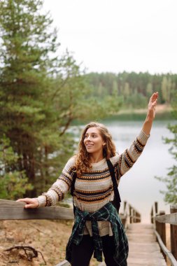 Göle bakan ahşap bir patikada genç bir kadın gezginin portresi. Sırt çantalı hoş bir kadın doğanın tadını çıkarıyor ve ormanda yürüyor. Macera, doğa konsepti.