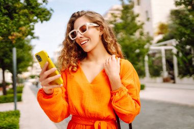 Parlak elbiseli şık bir kadın şehrin güneşli caddelerinde telefonla dolaşıyor. Güzel bir kadın dışarıda poz veriyor, bloglar ya da telefonda SMS yazıyor. Güzellik ve moda kavramı, modernlik.