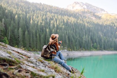 Sırt çantalı bir bayan yürüyüşçü güneşli bir günde bir gölün yakınındaki dağlık alanı keşfeder. Genç bayan gezgin dağ gölünün ve yoğun bir ormanla çevrili maceranın tadını çıkarıyor. Özgürlük kavramı, tatil.