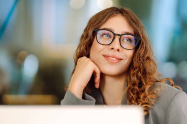 Gözlüklü güzel bir kadın güneşli bir günde bir terasta otururken dizüstü bilgisayarda çalışıyor. Diz üstü bilgisayarı olan serbest çalışan bir kadın açık havada rahat bir atmosferin tadını çıkarıyor. İş ve teknoloji kavramı.