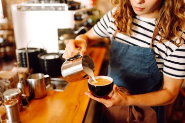 Deneyimli bir barista modern bir espresso makinesinde aromatik kahve hazırlar. Süt köpürten bir kadının elleri, sıcak bir kahve dükkanında espresso hazırlıyor. Küçük işletme konsepti, içkiler.