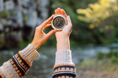 Dağın eteklerinde pusula tutan kadın yürüyüşçünün arka görüntüsü. Yürüyüş yapan güzel bir kadın yön bulmak için pusulaya bakıyor, araziyi keşfediyor. Macera konsepti, yürüyüş. Etkin yaşam biçimi.