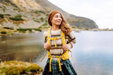 Sarı sırt çantalı, dağ gölü kenarında doğa ve özgürlüğün tadını çıkaran yürüyüşçü kadın. Dağlarda yürüyüş parkurunda güzel bir kadın. Macera konsepti, vahşi doğa.