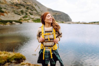 Sarı sırt çantalı, dağ gölü kenarında doğa ve özgürlüğün tadını çıkaran yürüyüşçü kadın. Dağlarda yürüyüş parkurunda güzel bir kadın. Macera konsepti, vahşi doğa.