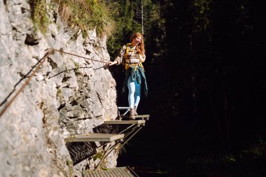 Sırt çantalı kadın yürüyüşçü dağlardaki yaya asma köprüsünde yürüyor. Genç bir kadın dağ manzarasından zevk alıyor ve açık havada özgürlüğü hissediyor. Seyahat, özgürlük kavramı.